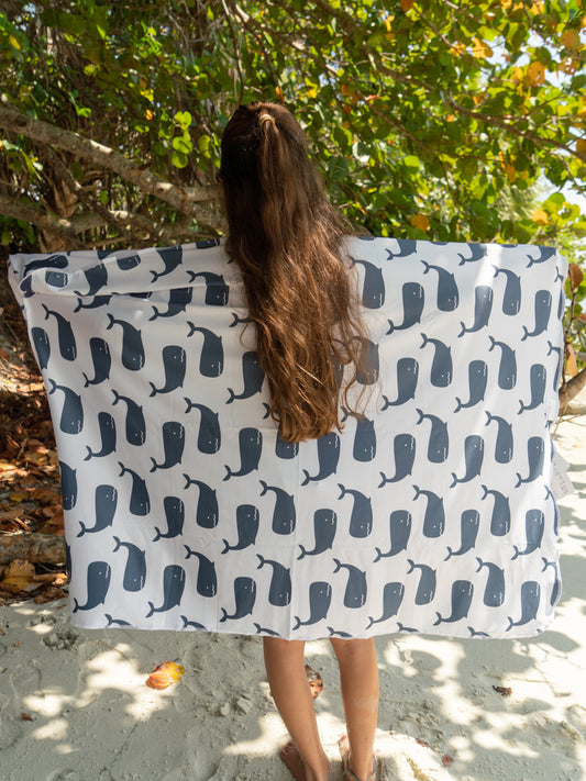 A person standing on a beach with a hooded sunscreen towel draped over their shoulders, featuring a blue and white animal pattern.