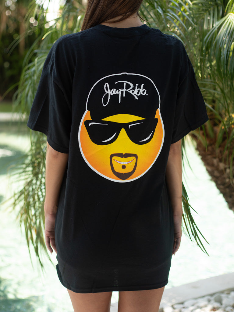 Woman wearing black t-shirt with an emoji on the back, standing by a body of water.