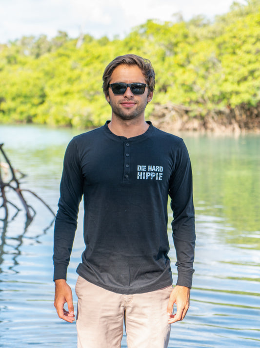 Man wearing a black long-sleeve shirt with text, standing outdoors by water
