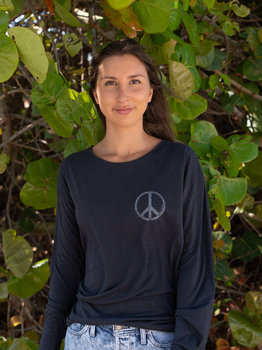 Woman standing by tree leaves wearing a black long-sleeve shirt with a peace symbol.