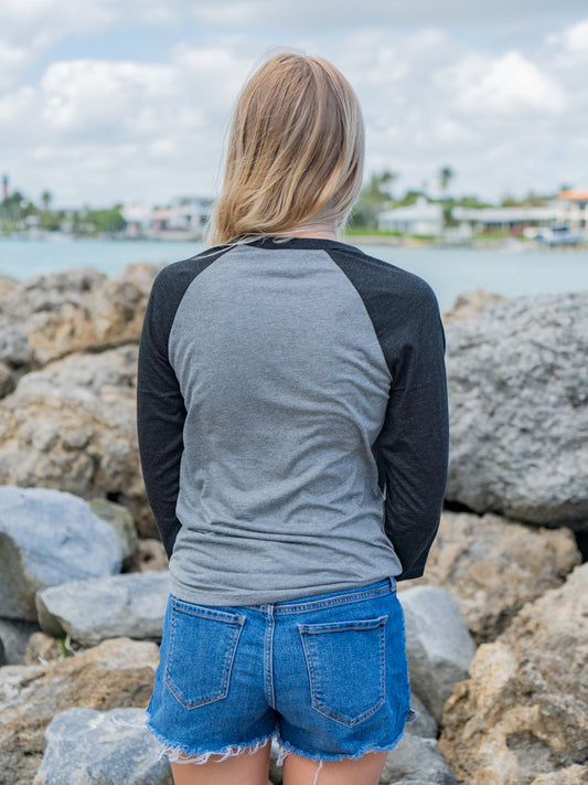 Woman wearing a 'No Worries' shirt standing in front of rocks and the ocean.