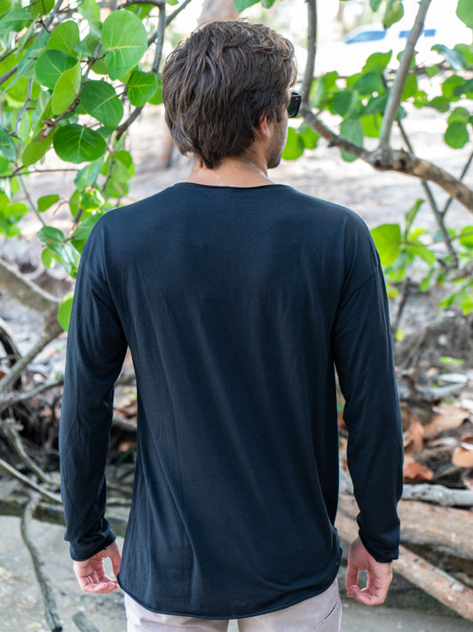 Man standing among tree branches wearing a black long-sleeve shirt and light gray shorts.