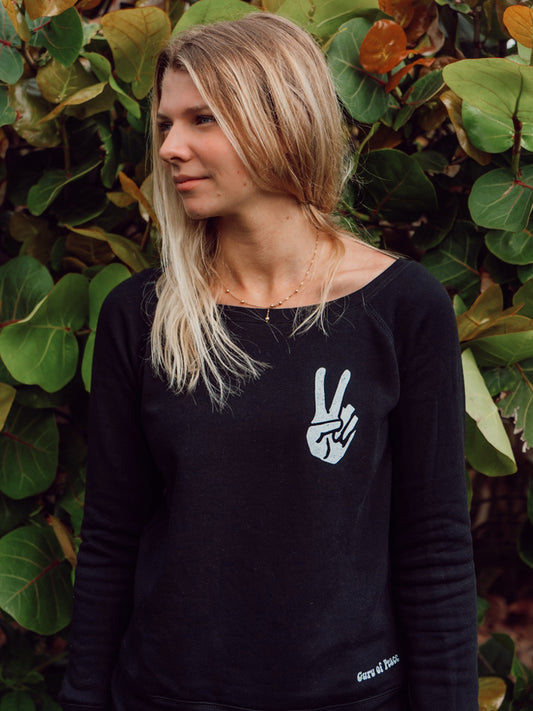 Woman wearing a black sweatshirt with a peace sign design, standing in front of green foliage.