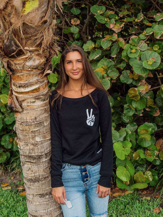 Woman wearing a black sweatshirt with a peace sign design, standing in front of green foliage.