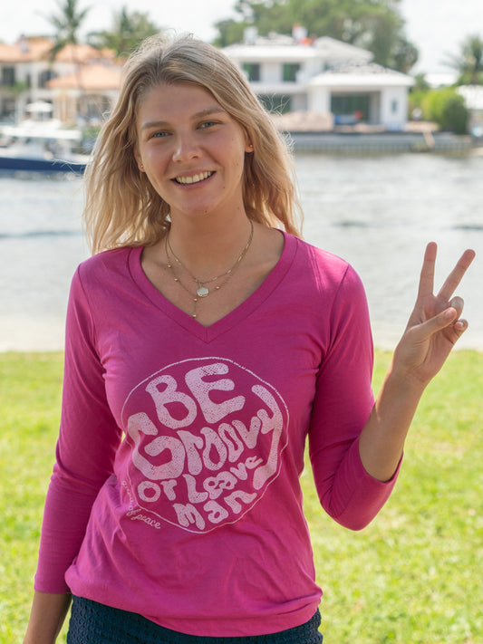Woman wearing a pink long-sleeve shirt with a graphic design by a body of water.