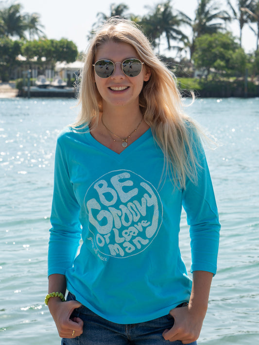 Woman wearing a turquoise long-sleeve shirt with a graphic design by a body of water.