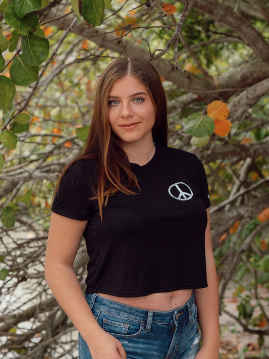 Woman wearing a black cropped t-shirt with a peace symbol on a beach