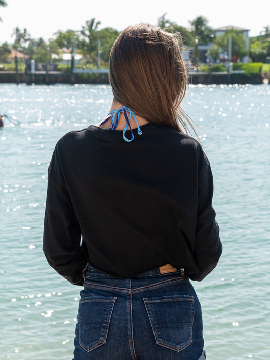 Woman wearing a black long-sleeve crop top, standing by a body of water