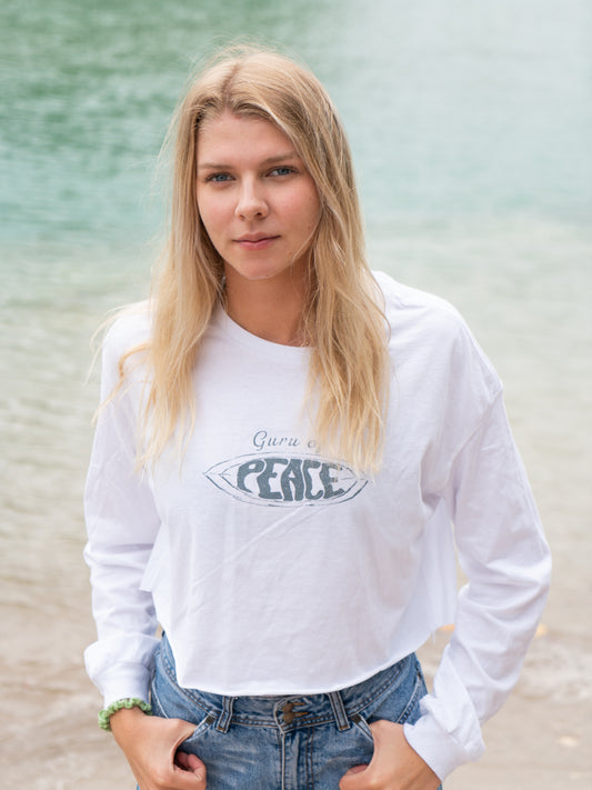 Woman wearing a white long-sleeve crop top with a logo and text, standing on a beach