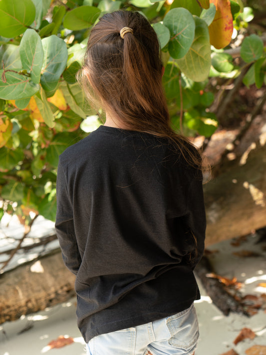 Young girl wearing a black long-sleeve shirt, standing on a beach.
