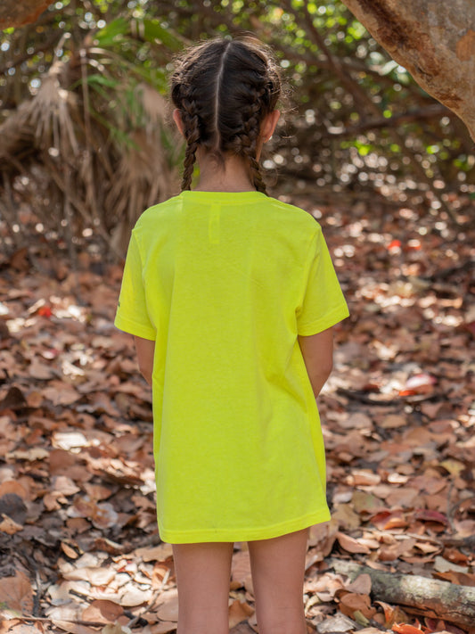 Young girl standing by a tree branch wearing a yellow t-shirt.