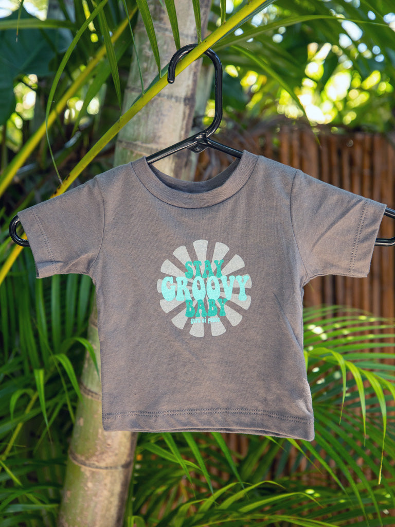 Black t-shirt with 'Stay Groovy Baby' design on a hanger against a green leafy background