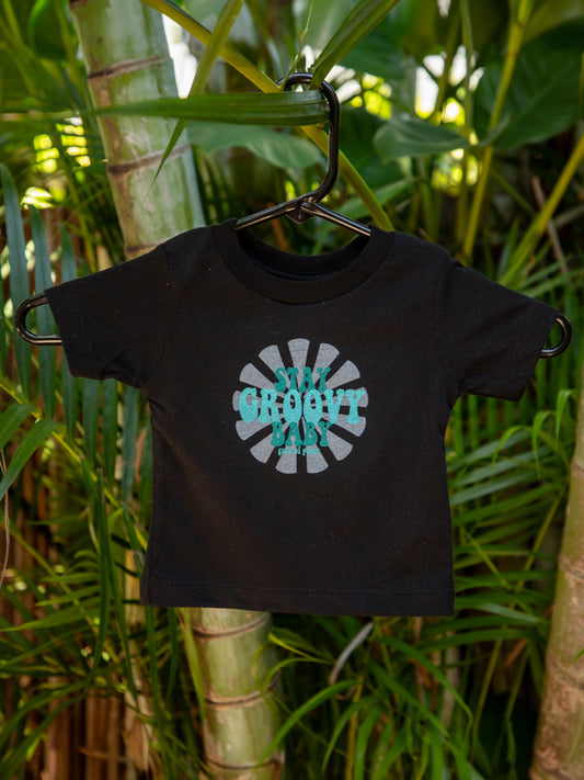 Black t-shirt with 'Stay Groovy Baby' design on a hanger against a green leafy background