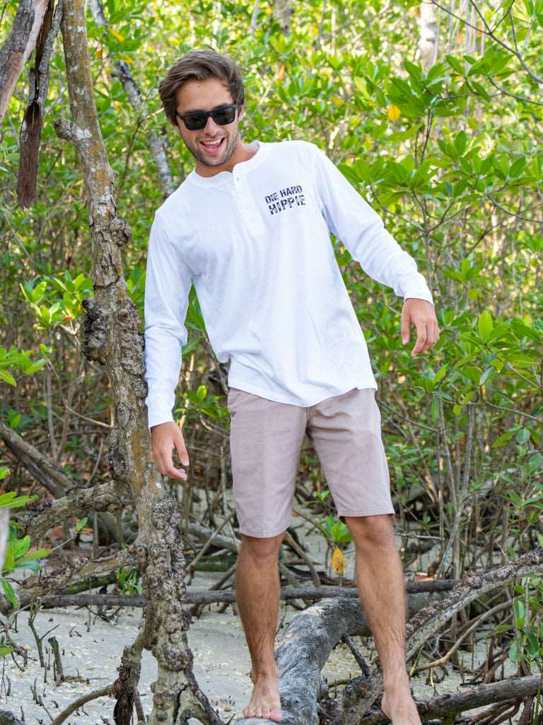 Man wearing a white long-sleeve shirt with text, standing outdoors among greenery.