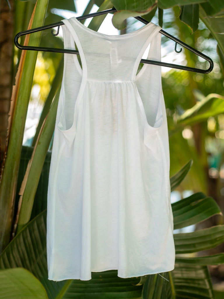 White tank top on a hanger against a leafy green background.