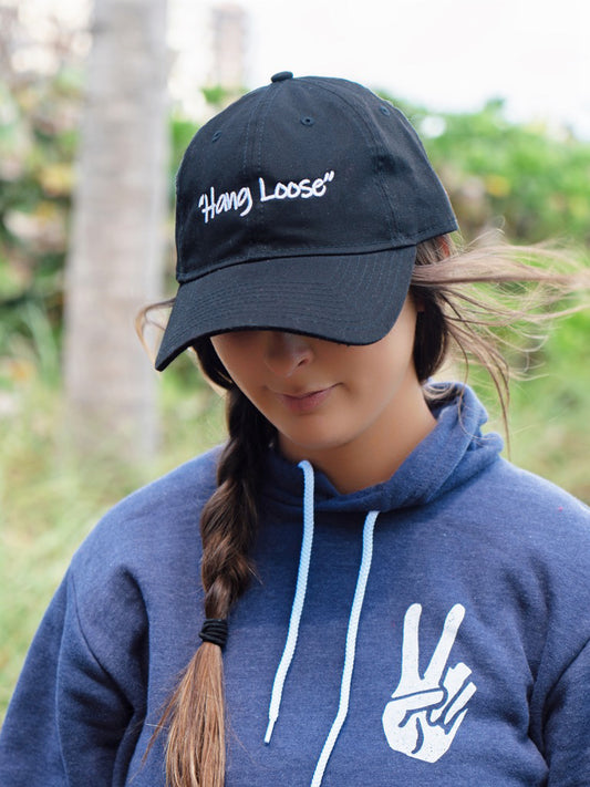 Person wearing a black cap with 'Hang Loose' text and a blue hoodie with a peace sign design.