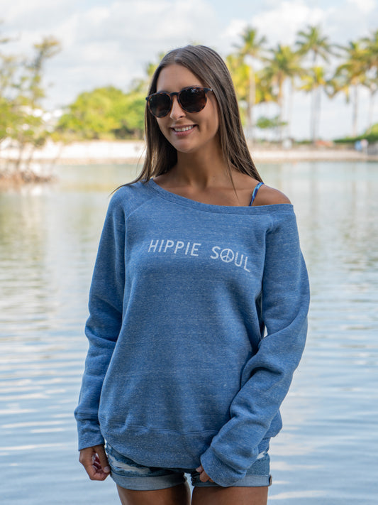 Woman wearing a blue 'Hippie Soul' sweatshirt by a lake with palm trees in the background.