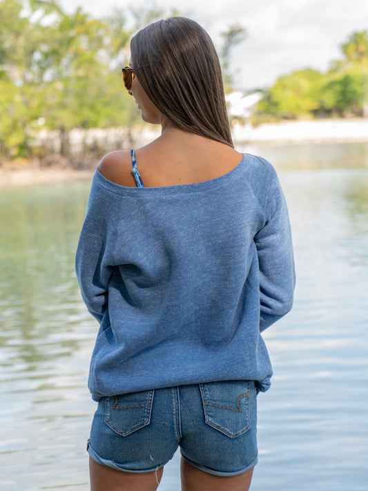 Woman wearing a wide neck blue crewneck by a body of water