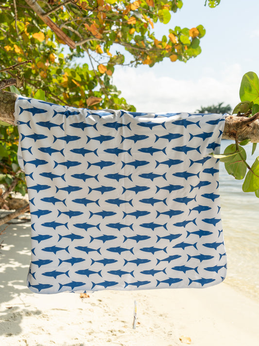 Towel hanging on tree branch with shark pattern on the beach.