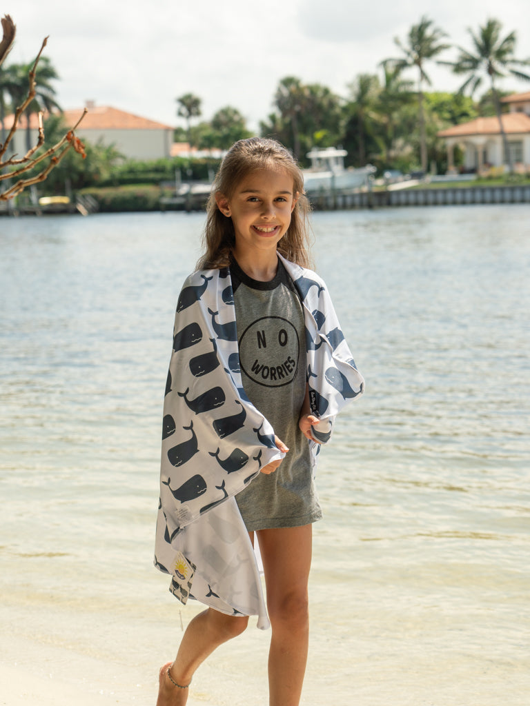 Person holding a large towel with whale pattern on a beach