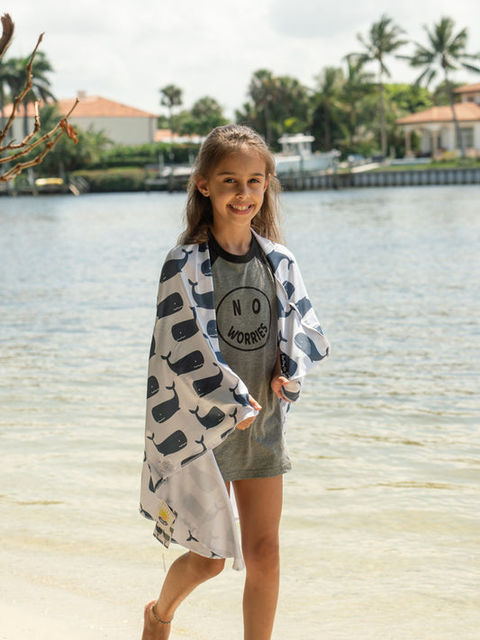 Person holding a large towel with whale pattern on a beach