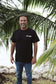 Man wearing a black t-shirt with 'JAY ROBB' text, standing in front of palm trees.