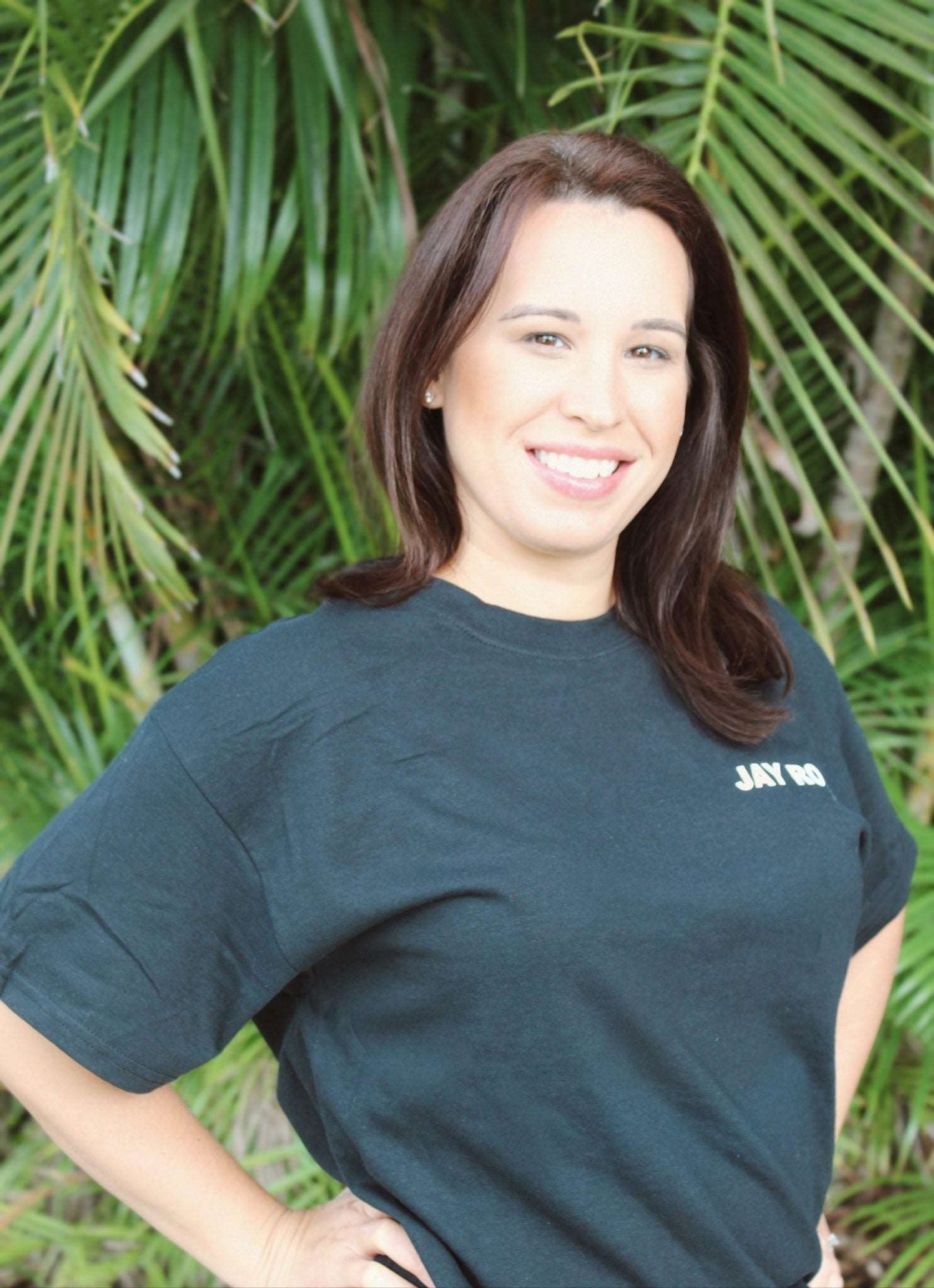 Woman wearing black Jay Robb Emoji Tee, standing with a leafy background