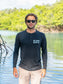 Man wearing a black long-sleeve shirt with text, standing outdoors by water