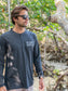 Man wearing a grey long-sleeve shirt with text, standing outdoors with trees in the background.