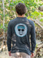 Man wearing a grey long-sleeve shirt with logo, standing outdoors with trees in the background.