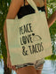Person holding a beige tote bag with 'peace love & tacos' text against a blurred natural background