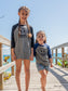 Children standing on a wooden boardwalk by the ocean