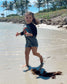 Child in a grey shirt with a colorful design standing on a sandy beach with palm trees in the background