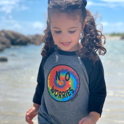 Child in a grey shirt with a colorful design standing on a sandy beach with palm trees in the background