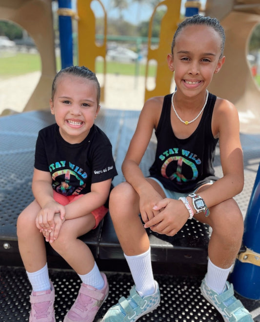 Two young girls sitting on a playground bench wearing matching 'Stay Wild' shirts.