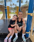 Two young girls sitting on a playground bench wearing matching 'Stay Wild' shirts.