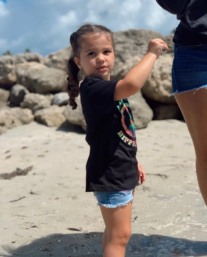 Young girl on the beach wearing black tee with the text 'Stay Wild'.