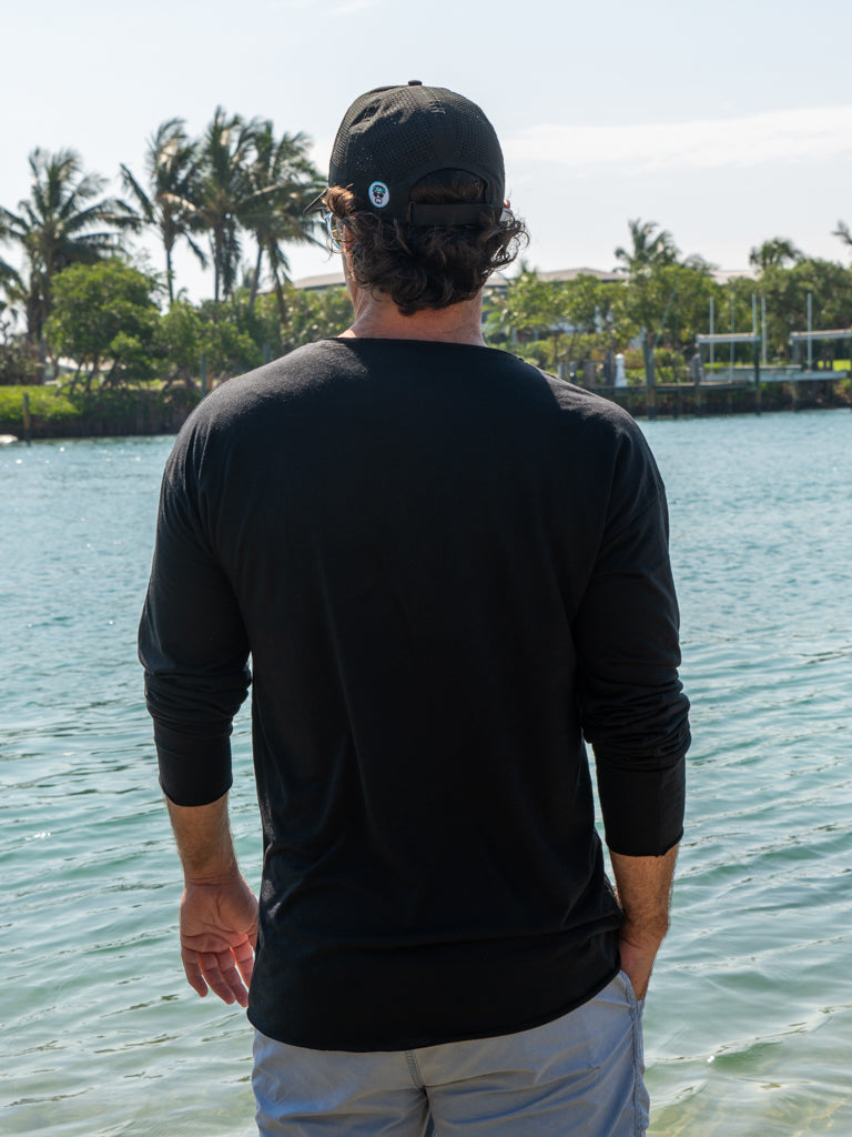 Man standing by a body of water wearing a black long-sleeve shirt.