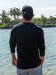 Man standing by a body of water wearing a black long-sleeve shirt.