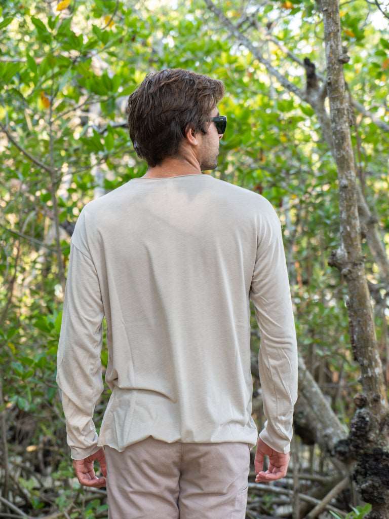Man standing among tree branches wearing a tan long-sleeve shirt and light brown shorts.