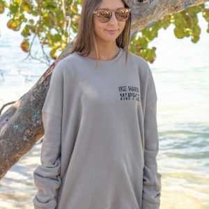 Woman wearing a gray sweatshirt with text, standing by a tree on a beach.