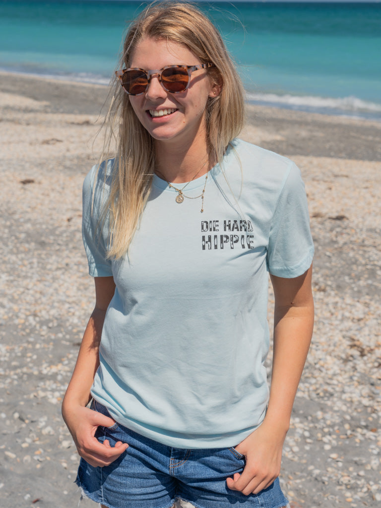 Woman standing by a beach wearing a light blue t-shirt with a logo
