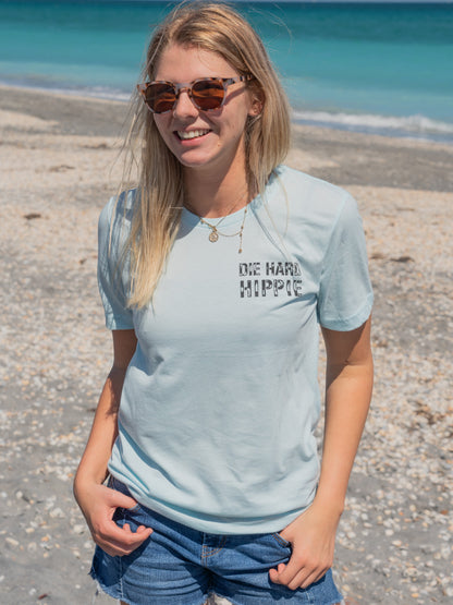 Woman standing by a beach wearing a light blue t-shirt with a logo