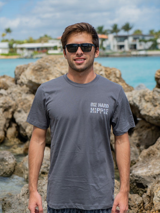 Man wearing a gray t-shirt with the words 'Die Hard Hippie', standing by rocks and water.