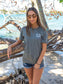 Woman wearing a gray t-shirt with the words 'Die Hard Hippie', standing by rocks and water.