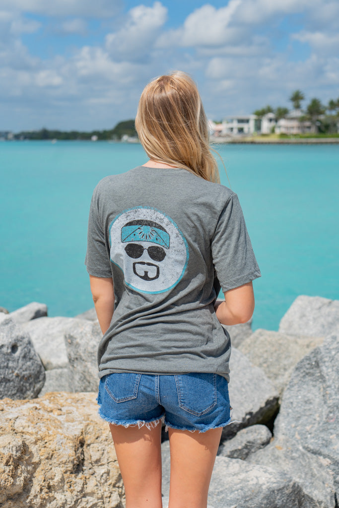 Woman wearing a gray t-shirt with a logo, standing by rocks and water.