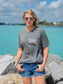 Woman wearing a gray t-shirt with the words 'Die Hard Hippie', standing by rocks and water.