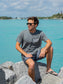 Man wearing a gray t-shirt with the words 'Die Hard Hippie', sitting on rocks by water.
