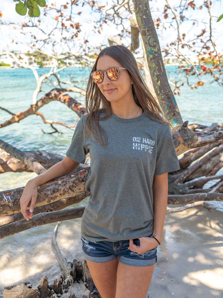 Woman wearing a gray t-shirt with the words 'Die Hard Hippie', standing by rocks and water.