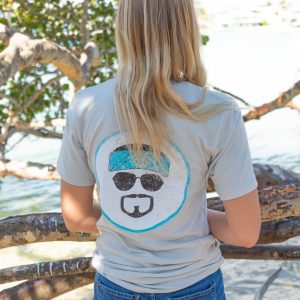 Woman wearing a gray t-shirt with text and graphics, standing on rocks by a body of water.
